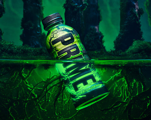 PRIME Glowberry hydration drink bottle partially submerged in glowing green water, set against a dark, eerie forest background. The bottle's glow-in-the-dark design is emphasized, highlighting the PRIME branding and the unique Glowberry flavor.